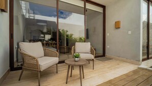 Un'ampia terrazza con due poltrone in vimini e un tavolino rotondo, una porta vetrata scorrevole che dà su un balcone e vista sul cielo e sul verde circostante.