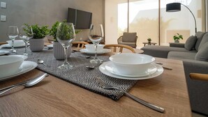 Un'area pranzo con un tavolo apparecchiato per quattro, comprensivo di piatti, bicchieri e posate. Sul tavolo ci sono piante in vaso, un televisore montato a parete e un divano sullo sfondo.