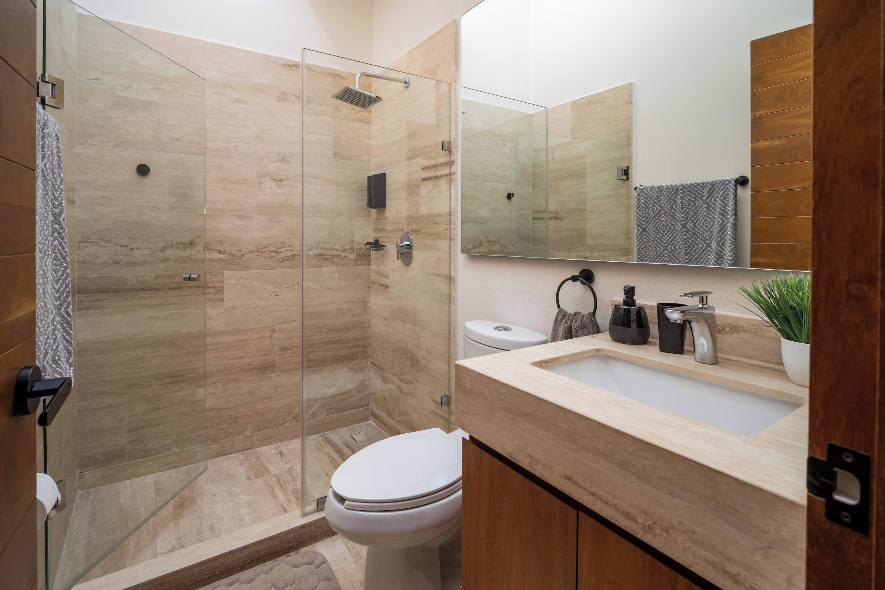 Et moderne badeværelse med bruseniche, toilet, vask med spejl og en potteplante.