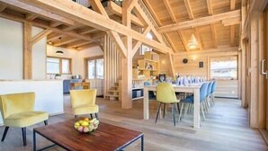 Una habitación amplia con techo de madera, comedor con sillas y mesa, y zona de cocina con armarios y encimera.