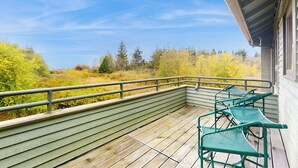 A wooden deck with green metal chairs and a railing overlooking a natural landscape with trees and bushes. - 2 BR Home Surrounded by Tranquility (Lummi Island)