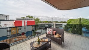 A balcony with wicker furniture, a bottle, and glasses, overlooking a cityscape with buildings and greenery. - Super Villaggio Planetarium Resort one Bedroom Apartment Sleeps 4 (San Michele al Tagliamento)