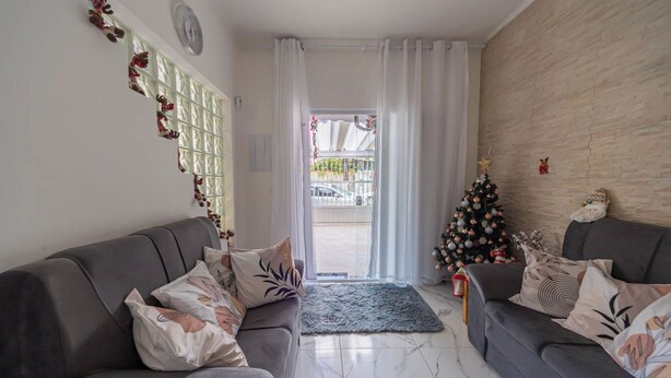 A living room with two grey sofas, a small Christmas tree, and a patterned rug. - Casa Pet Friendly com Wi-fi e Garagem no Ocian (Praia Grande)
