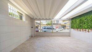 A clean, tiled hallway with a gated entrance, a green wall with plants, and a view of parked cars outside. - Casa Pet Friendly com Wi-fi e Garagem no Ocian (Praia Grande)