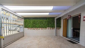 A spacious indoor area with a tiled floor, a green wall with hanging decorations, and a metal gate. - Casa Pet Friendly com Wi-fi e Garagem no Ocian (Praia Grande)