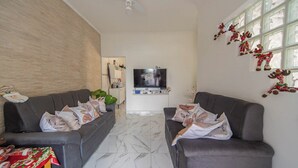 A modern living room with two grey sofas, a flat-screen TV, and a decorative wall with reindeer figures. - Casa Pet Friendly com Wi-fi e Garagem no Ocian (Praia Grande)
