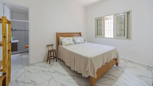 A bedroom with a bed, a wooden chair, a window with shutters, and a ceiling fan. - Casa Pet Friendly com Wi-fi e Garagem no Ocian (Praia Grande)