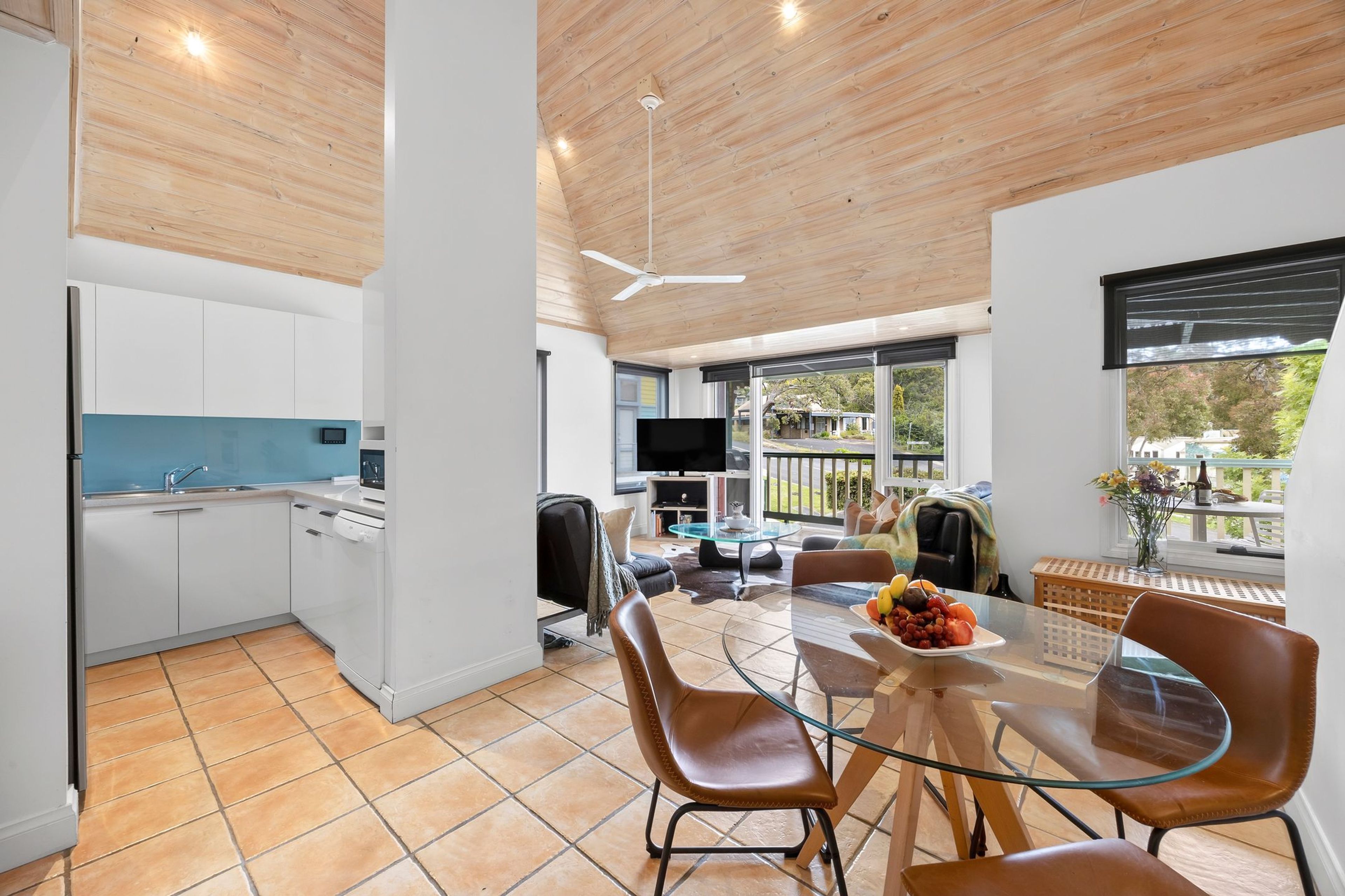 Una cocina moderna con armarios blancos, encimera azul y una zona de comedor con mesa de vidrio y sillas de cuero.