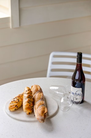 A table with a bottle of wine, two glasses, and a plate with three pastries. - Cora Lynn 14 (Lorne)