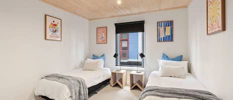 A bedroom with two beds, a window, and artwork on the walls.