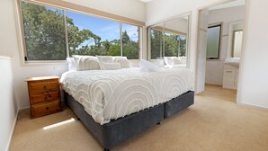 Een slaapkamer met een groot bed, een houten dressoir en een badkamer door een open deur zichtbaar.