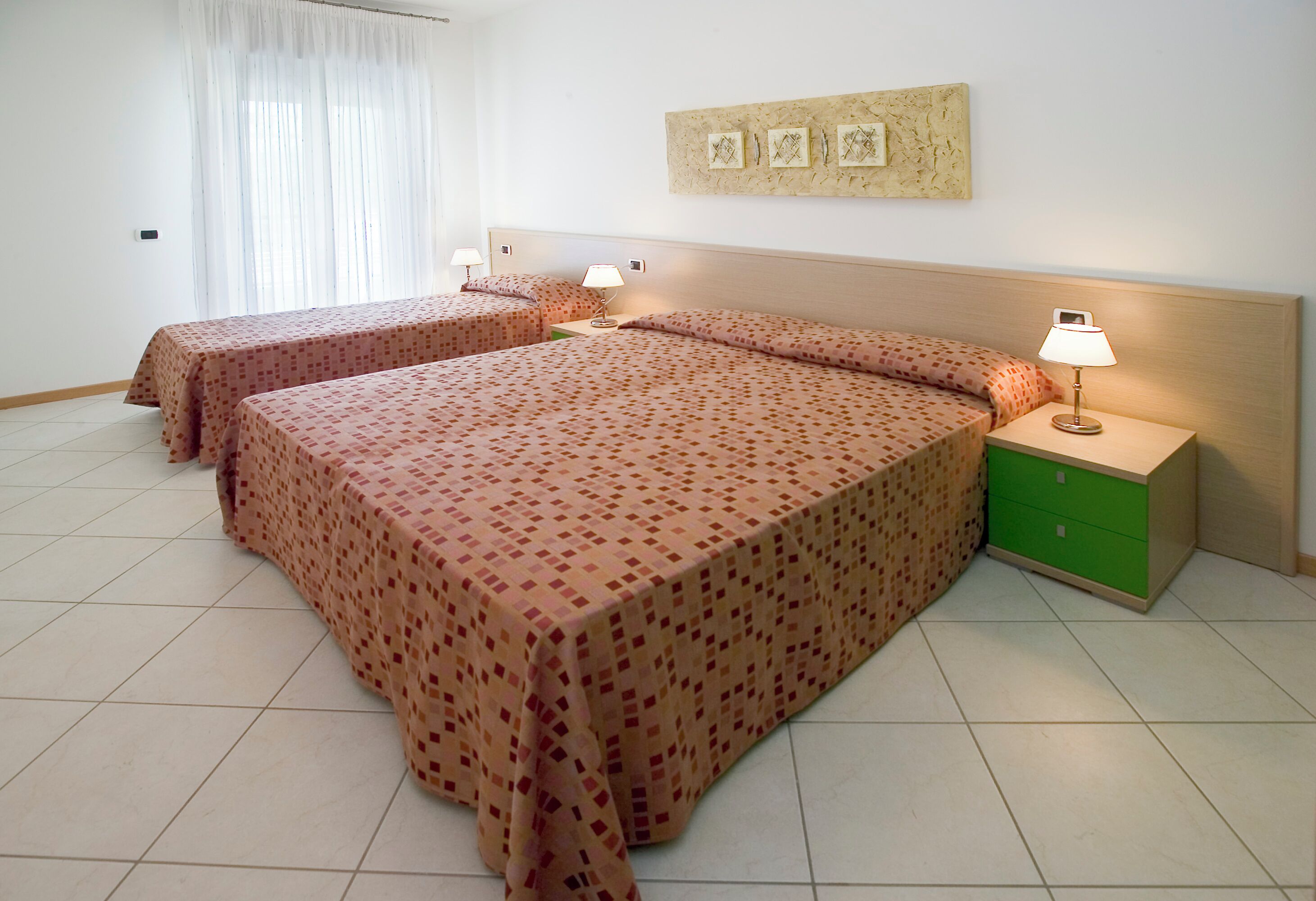 Ein Hotelzimmer mit zwei Betten, einem grünen Nachttisch und einer Wandlampe.