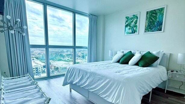 Un dormitorio moderno con una cama grande, un tendedero y vistas a la ciudad a través de amplios ventanales.