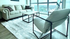 Una sala moderna con un sofá, una mesa de centro y una silla. Una ventana grande ofrece vistas de la ciudad.