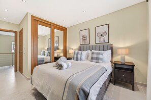 A bedroom with a bed, bedside tables, a mirror, and framed artwork on the wall. - Townhouse Sasha (Almancil)