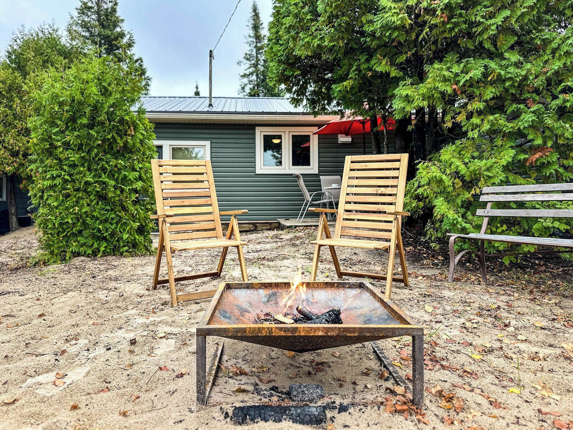 A rustic outdoor seating area with two wooden chairs and a metal fire pit.