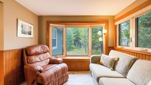 Une pièce chaleureuse avec un fauteuil en cuir, un canapé confortable et une grande fenêtre donnant sur une zone boisée.