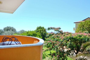 A balcony with a curved orange wall, a clear blue sky, and a view of a garden with pink flowering trees. - Apartment Near the Beach With Garden (Umag)