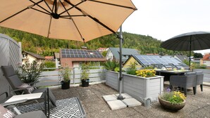 Un patio al aire libre con una mesa, sillas, un gran paraguas y paneles solares en el techo.
