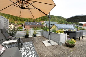 An outdoor patio with a table and chairs, a large umbrella, and solar panels on the roof. - Apartment in the Cathedral City, Haus Barbara 1st Floor with Mountain View, Terrace & Wi-Fi (St. Blasien)