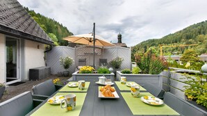 Un patio con una mesa dispuesta para una comida, rodeado de follaje y vistas a un edificio con cúpula.