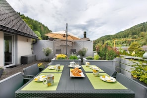A patio with a table set for a meal, surrounded by greenery and a view of a building with a dome. - Apartment in the Cathedral City, Haus Barbara 1st Floor with Mountain View, Terrace & Wi-Fi (St. Blasien)