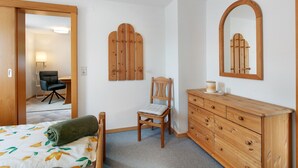 A bedroom with a bed, a wooden dresser, a chair, a mirror, and a door leading to another room. - Apartment in the Cathedral City, Haus Barbara 1st Floor with Mountain View, Terrace & Wi-Fi (St. Blasien)