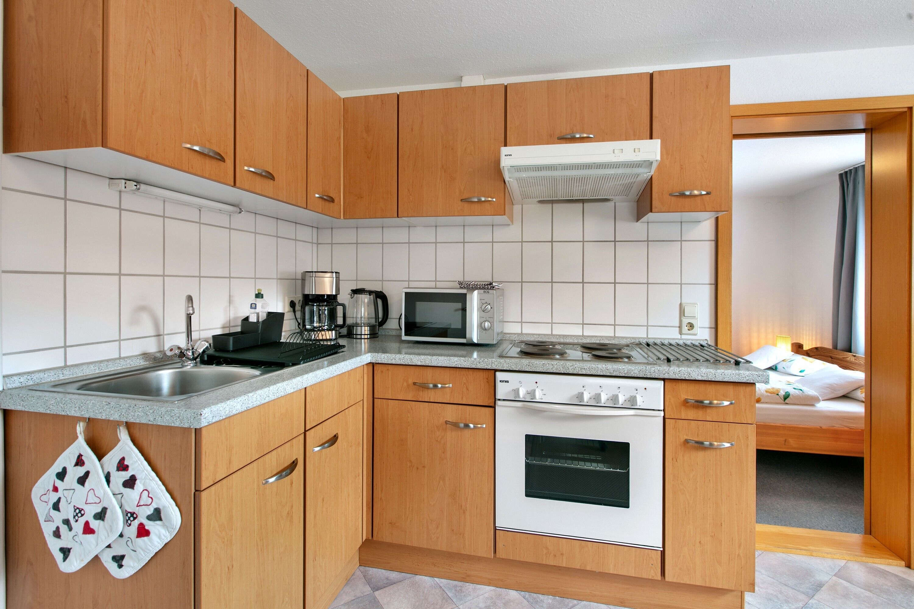 Una cocina compacta con armarios de madera, un microondas, un hervidor y un horno.