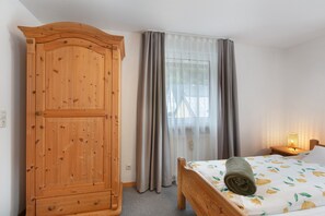 A bedroom with a wooden wardrobe, a bed with a rolled towel, a nightstand with a lamp, and sheer curtains. - Apartment in the Cathedral City, Haus Barbara 1st Floor with Mountain View, Terrace & Wi-Fi (St. Blasien)
