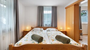 Una cama doble con cabecera de madera, dos mesitas de noche con lámparas y vista a una zona residencial por la ventana.