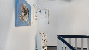 A hallway with a white wall, a blue painting, a small white cabinet, and a black railing. - Apartment in the Cathedral City, Haus Barbara 1st Floor with Mountain View, Terrace & Wi-Fi (St. Blasien)