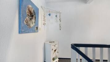 A hallway with a white wall, a blue painting, a small white cabinet, and a black railing.