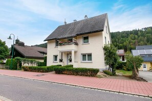A two-story building with a tiled roof, a balcony with potted plants, and a paved driveway. - Apartment in the Cathedral City, Haus Barbara 1st Floor with Mountain View, Terrace & Wi-Fi (St. Blasien)