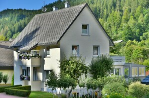 Un bâtiment à deux étages, doté d’un toit en pente, de nombreuses fenêtres et d’un balcon orné de fleurs.