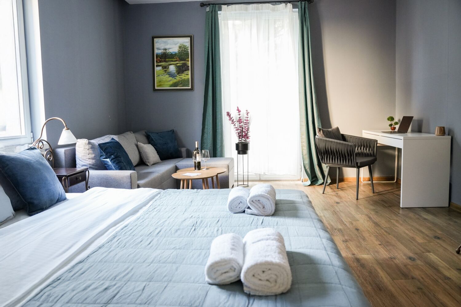 Une chambre d’hôtel moderne, dotée d’un grand lit, d’un canapé, d’un bureau et offrant une vue sur un tableau représentant un paysage.