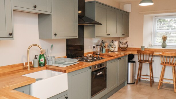 A kitchen with grey cabinets, a wooden countertop, a sink, a stove, and a window with blinds. - Starlight Cottage (Scarborough)