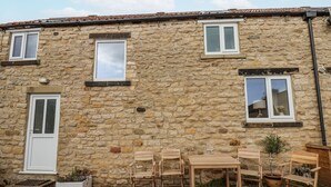 A stone building with a door, two windows, and a table with chairs outside. - Starlight Cottage (Scarborough)