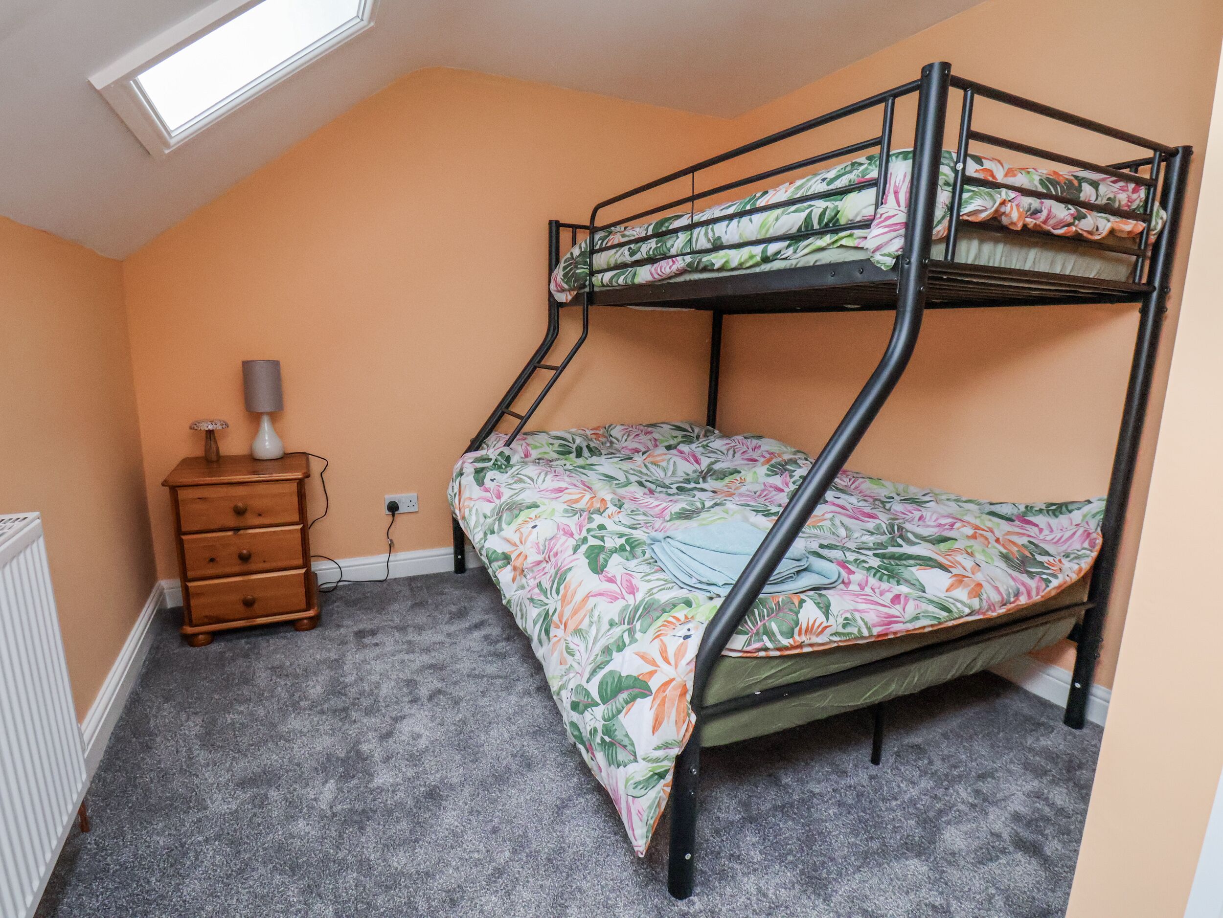 A bunk bed with a floral bedspread in a room with peach walls and a skylight.