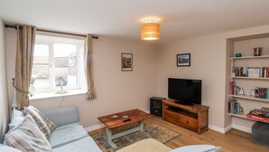 A living room with a sofa, a coffee table, a TV, and a bookshelf. - Starlight Cottage (Scarborough)