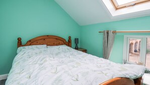 A bedroom with a wooden bed, a nightstand, a lamp, a window with a view of an outdoor area, and a skylight. - Starlight Cottage (Scarborough)