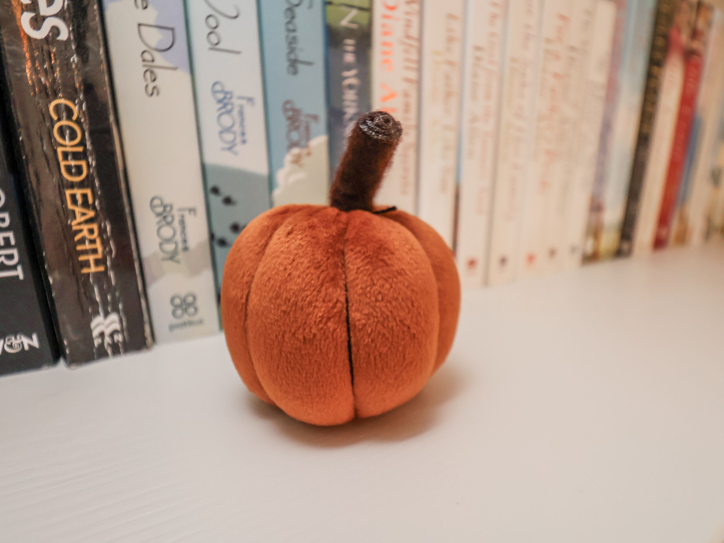 A plush pumpkin in front of a bookshelf filled with books.
