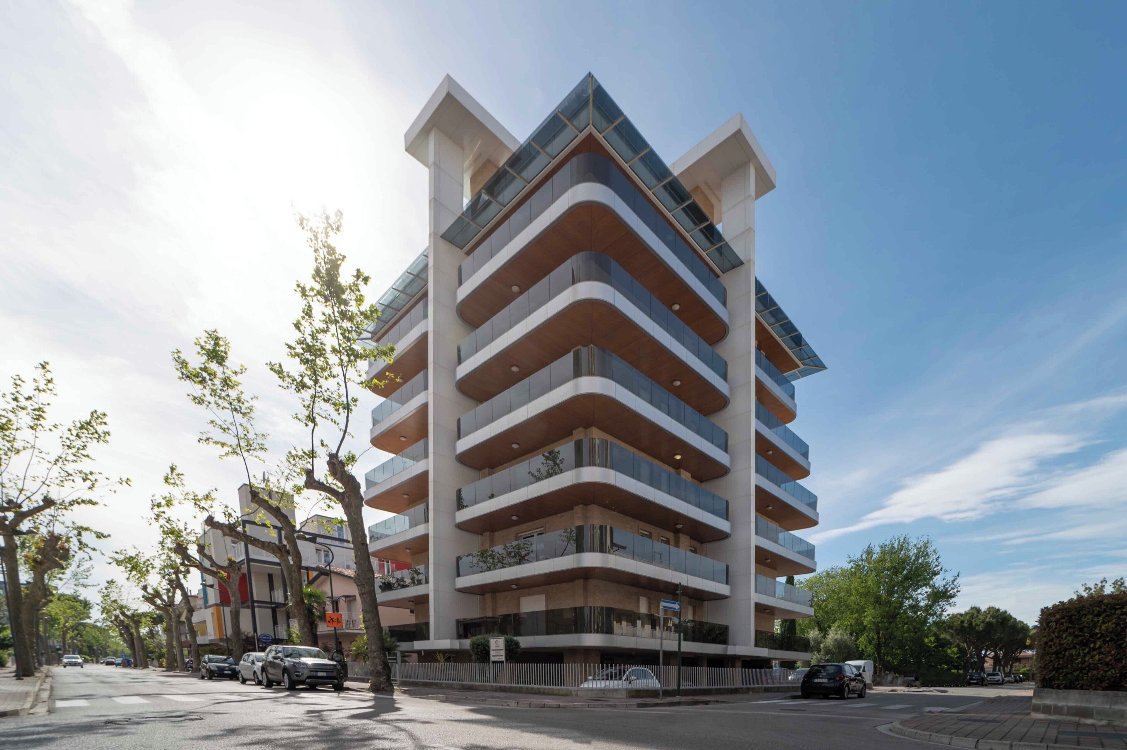 Een meerhoog gebouw met balkons, een heldere lucht en geparkeerde auto's op straat.