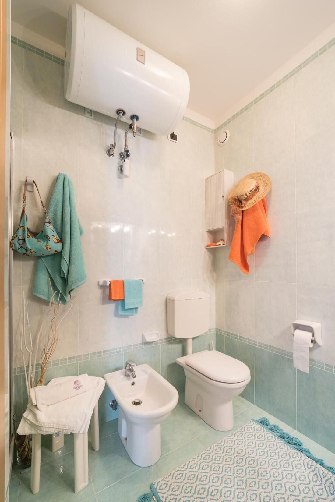 Ein Badezimmer mit Toilette, Bidet, Waschbecken, Handtuchhalter und Duschbereich.
