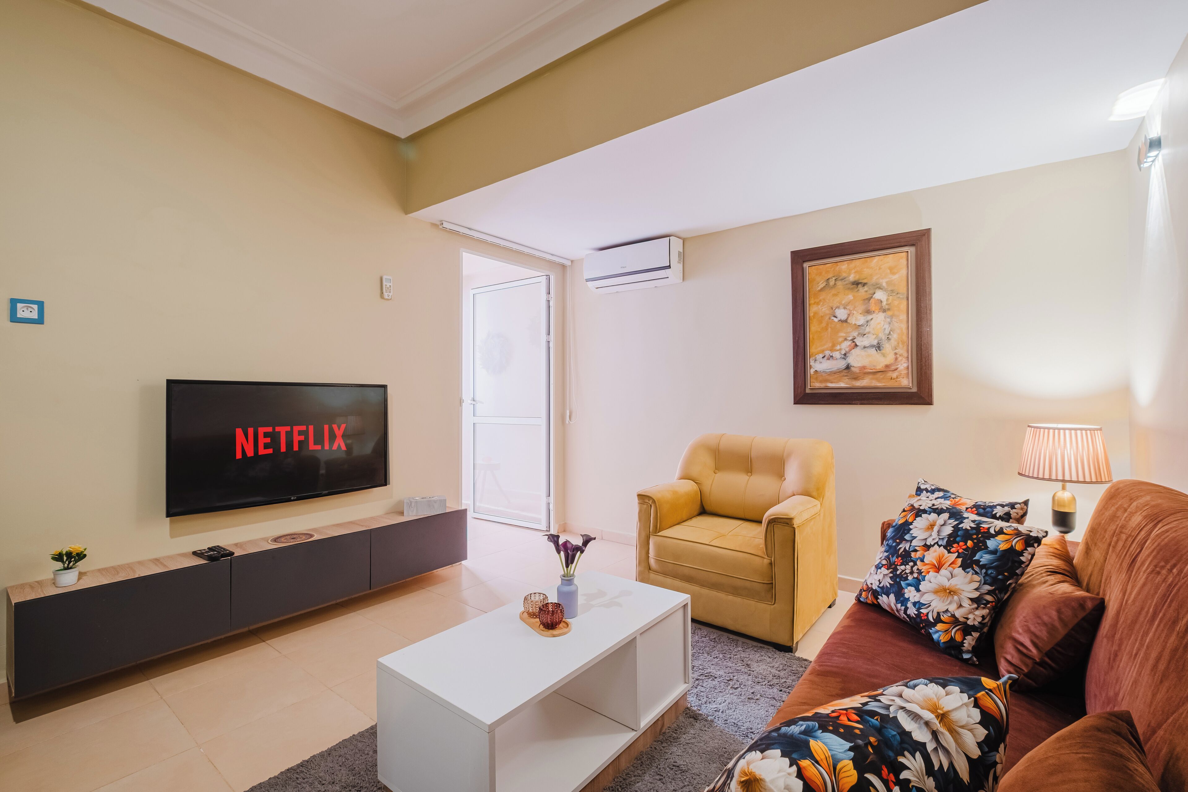 Ein Wohnzimmer mit Flachbildfernseher, der 'NETFLIX' anzeigt, einer Couch, einem Couchtisch und einem Sessel.