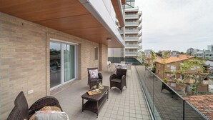Ein Balkon mit Korbmöbeln, einem Tisch mit Flasche und Gläsern sowie Blick auf eine Wohngegend.