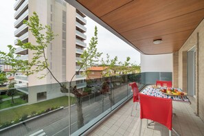 Un balcon avec une table dressée pour le dîner, une chaise rouge et une vue sur un paysage urbain avec des bâtiments et des arbres.