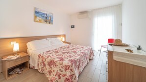 Ein Hotelzimmer mit Bett, Nachttischen, Schreibtisch, Stuhl und einem fensterbepflanzten Fenster.