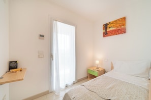 Une chambre à coucher avec un lit, une table de chevet, une lampe, un tableau et une porte avec des rideaux.