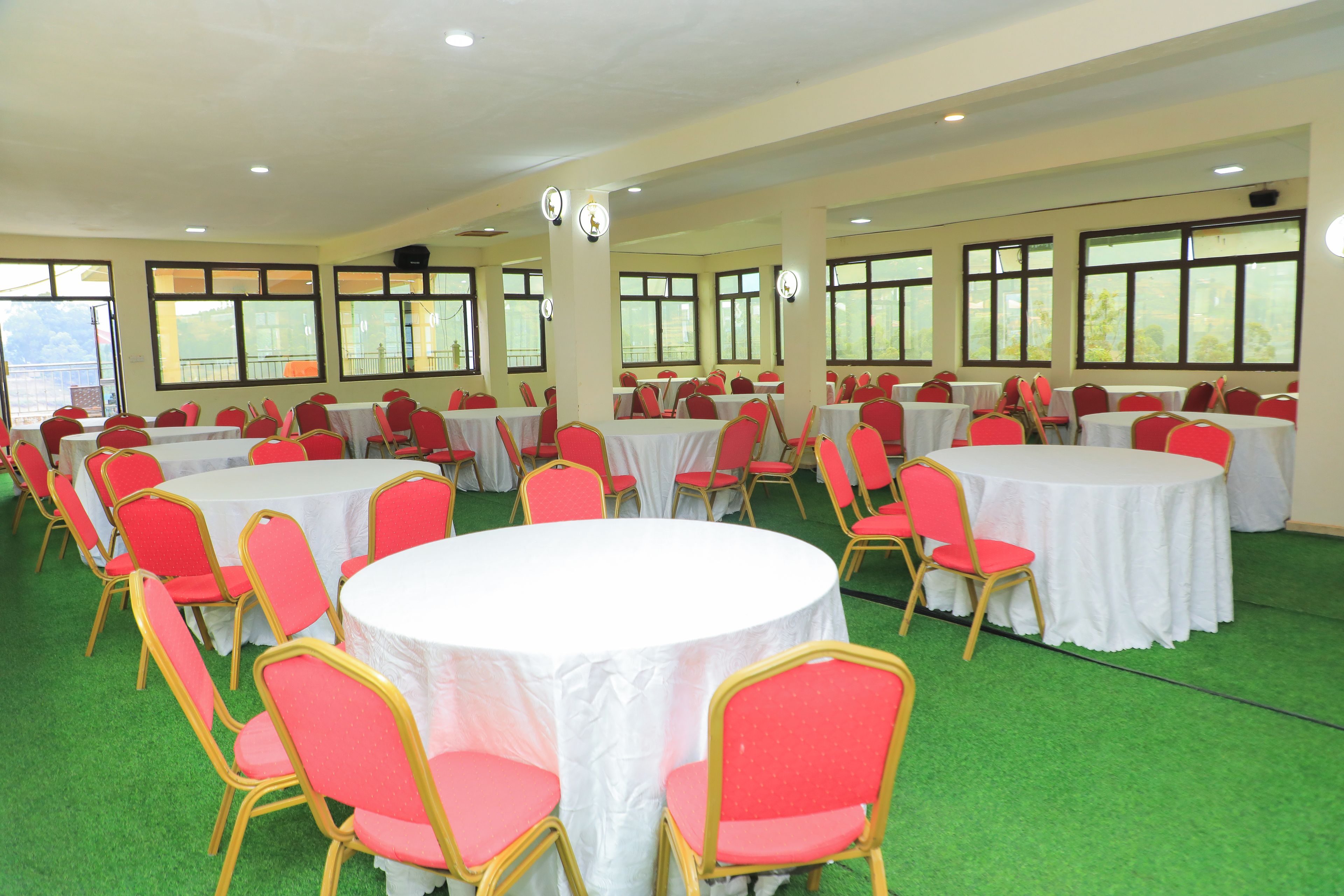A conference room with multiple round tables and red chairs, large windows, and a green carpet.