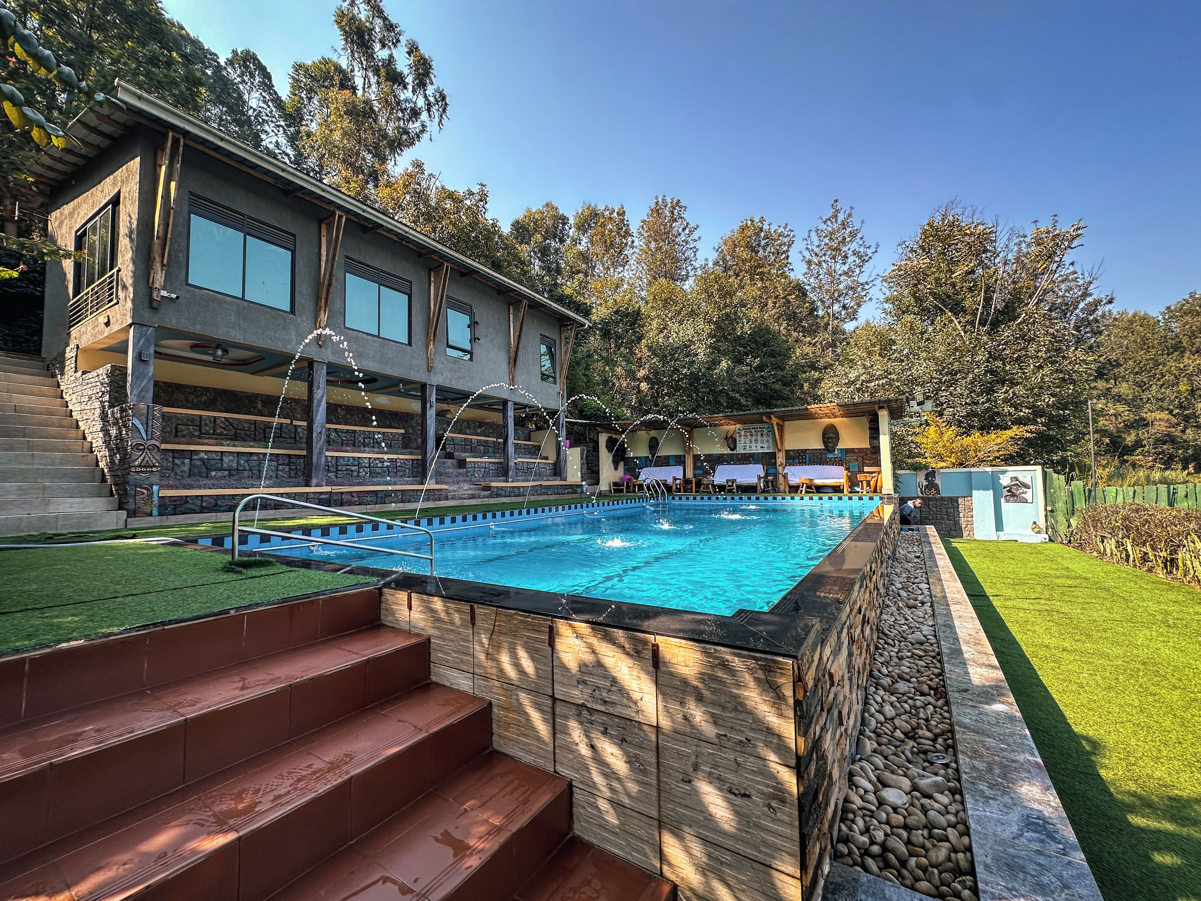 Una piscina con borde de piedra, una terraza de madera y un edificio con ventanas grandes.